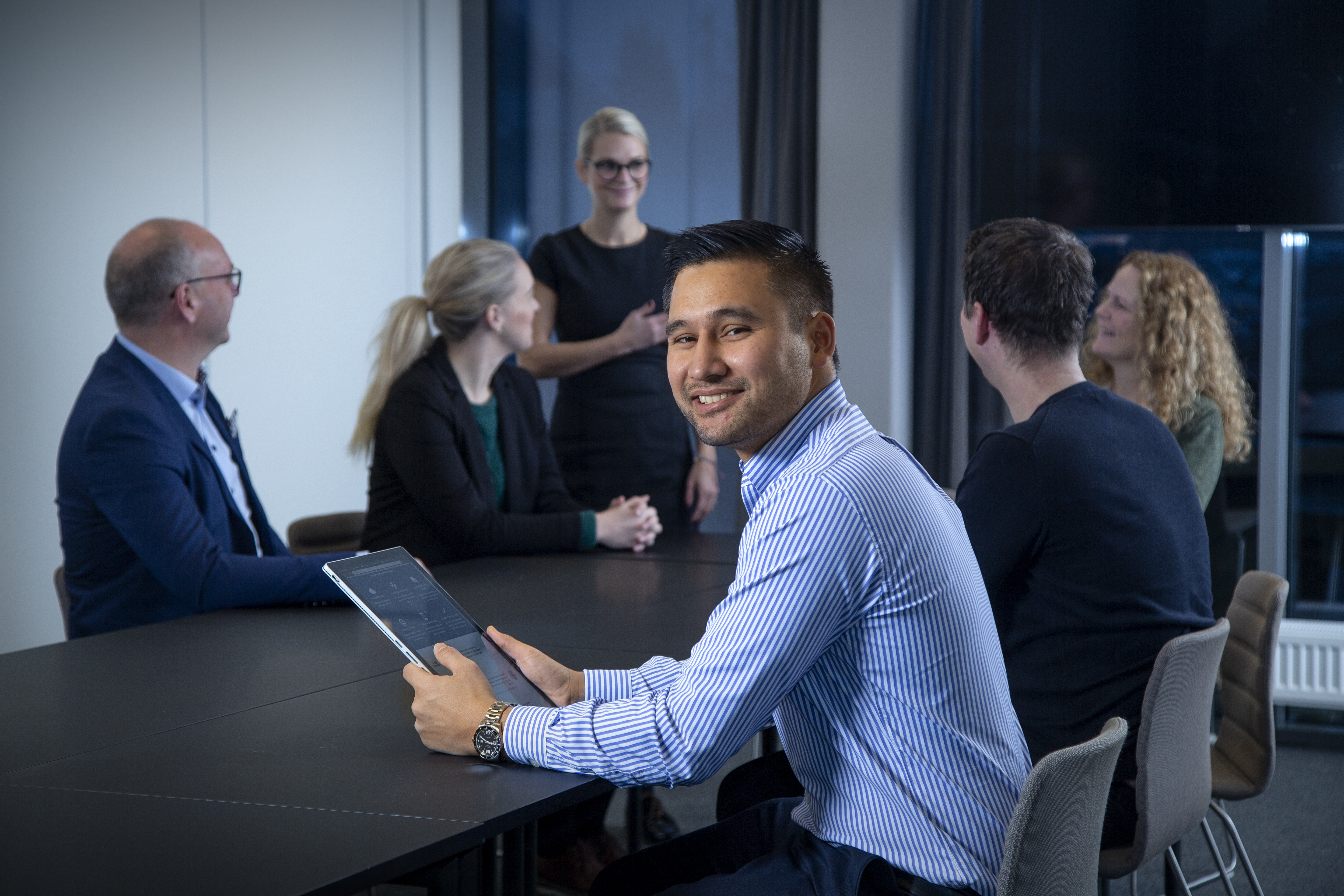 Man med tablet som sitter sammen med teamet sitt på kontoret.